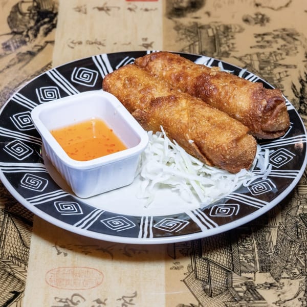 Three crispy golden egg rolls with shredded cabbage and a side of sweet chili sauce.