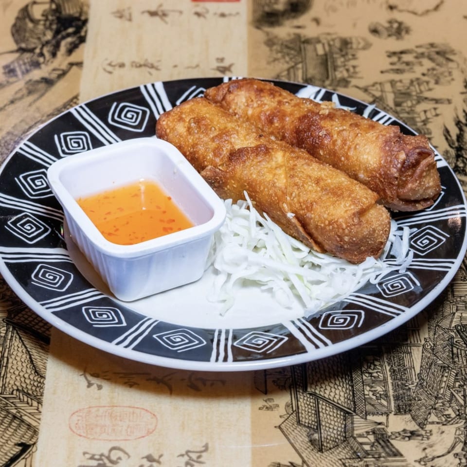 Three crispy golden egg rolls with shredded cabbage and a side of sweet chili sauce.