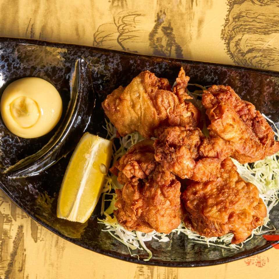 Crispy fried chicken karaage with shredded cabbage, a lemon wedge, and creamy sauce on a black plate.