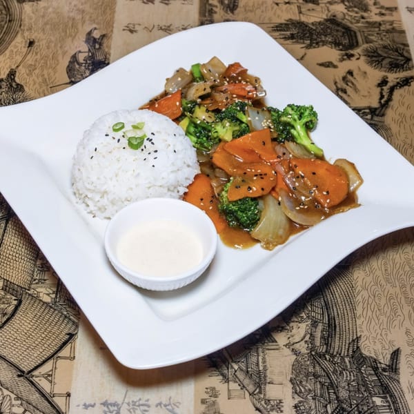 Stir-fried vegetables with broccoli, carrots, and onions, served with white rice and a side sauce.