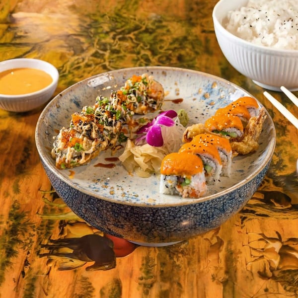 Two types of sushi rolls, one with orange sauce and the other with white sauce, on a decorative plate.
