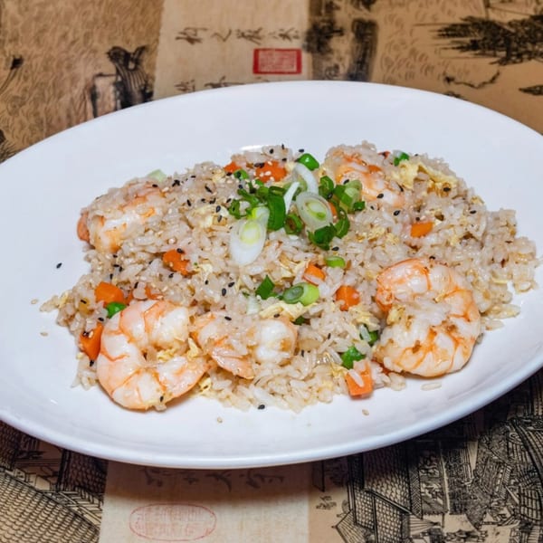 Shrimp fried rice with carrots, peas, egg, and green onions on a white plate.
