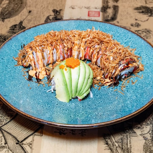 Sushi roll topped with crispy fried onions, drizzled sauce, and a fan of avocado with roe.