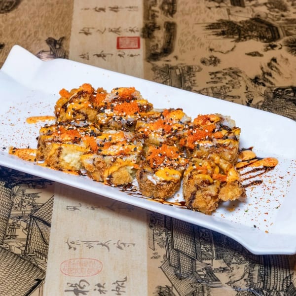 Crispy fried sushi rolls drizzled with orange sauce, black sesame seeds, and red roe on a white plate.