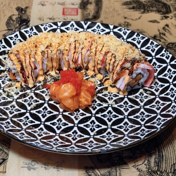 Sushi roll topped with crunchy breading, sauces, and a side of salmon and red roe.