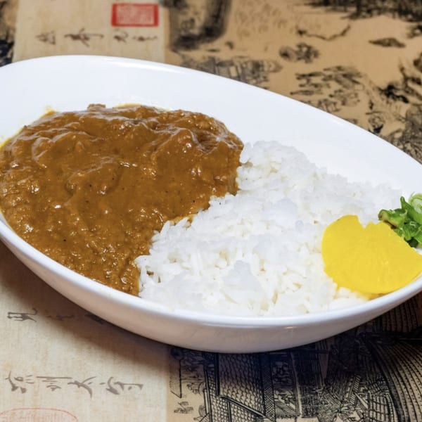 A white bowl of Japanese curry with white rice, yellow pickled daikon, and green onions.