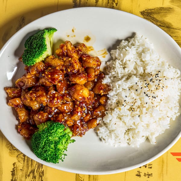Orange chicken with white rice and broccoli florets on a white plate.