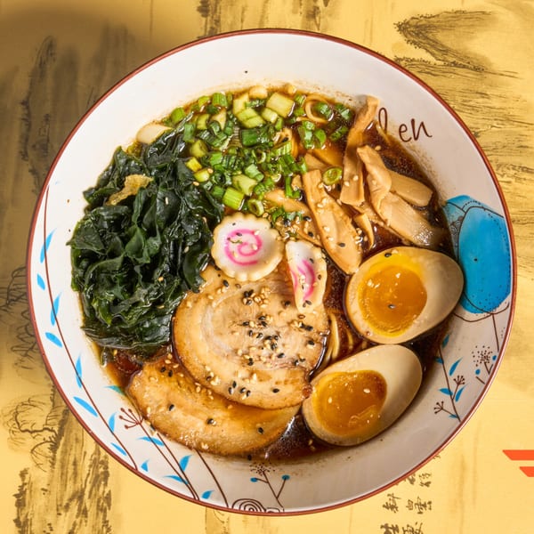 Overhead view of a ramen bowl with pork, eggs, seaweed, scallions, and bamboo shoots.