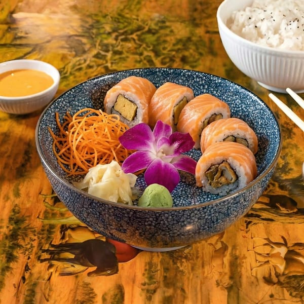 Salmon sushi rolls with pickled ginger, wasabi, shredded carrots, and an orchid in a blue bowl.