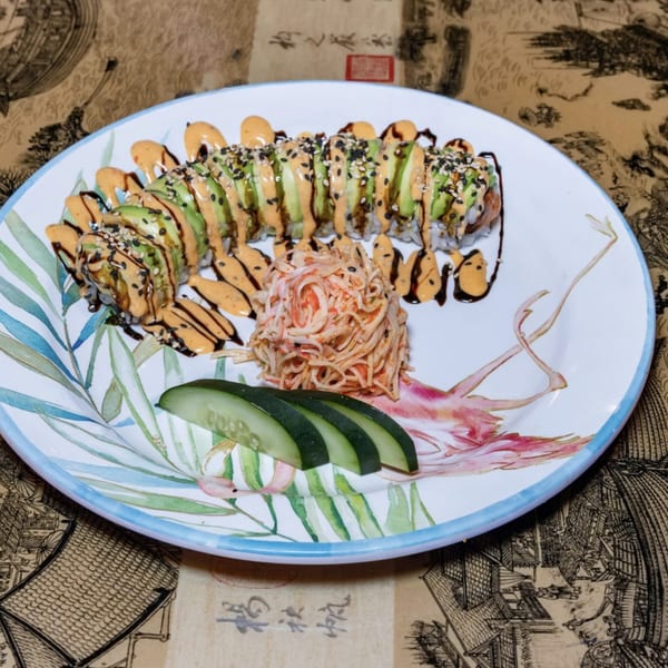 Dragon Roll sushi with avocado, spicy mayo, eel sauce, sesame seeds, and a side of crab salad.